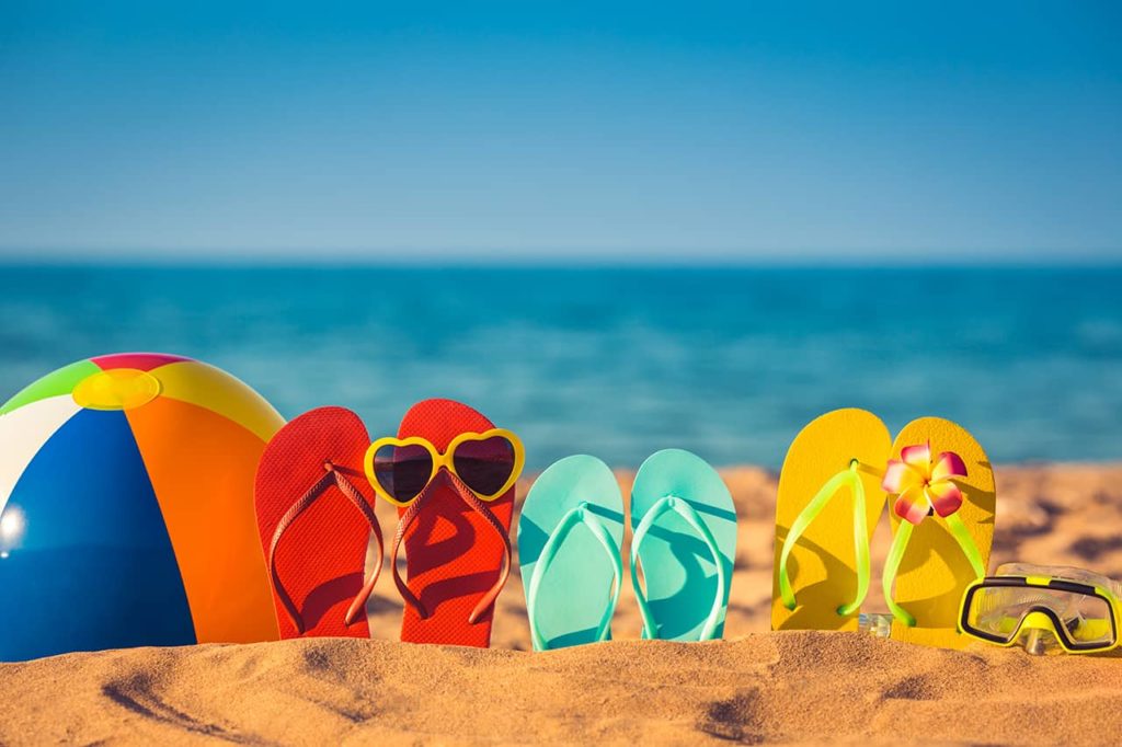 flip flops with sunglasses and a beach ball on the sand